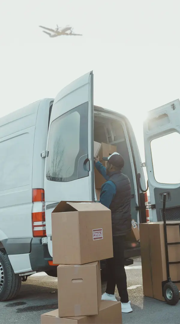 Worker loading cargo boxes into delivery van with aircraft overhead, representing Conquest Air Cargo's end-to-end freight service